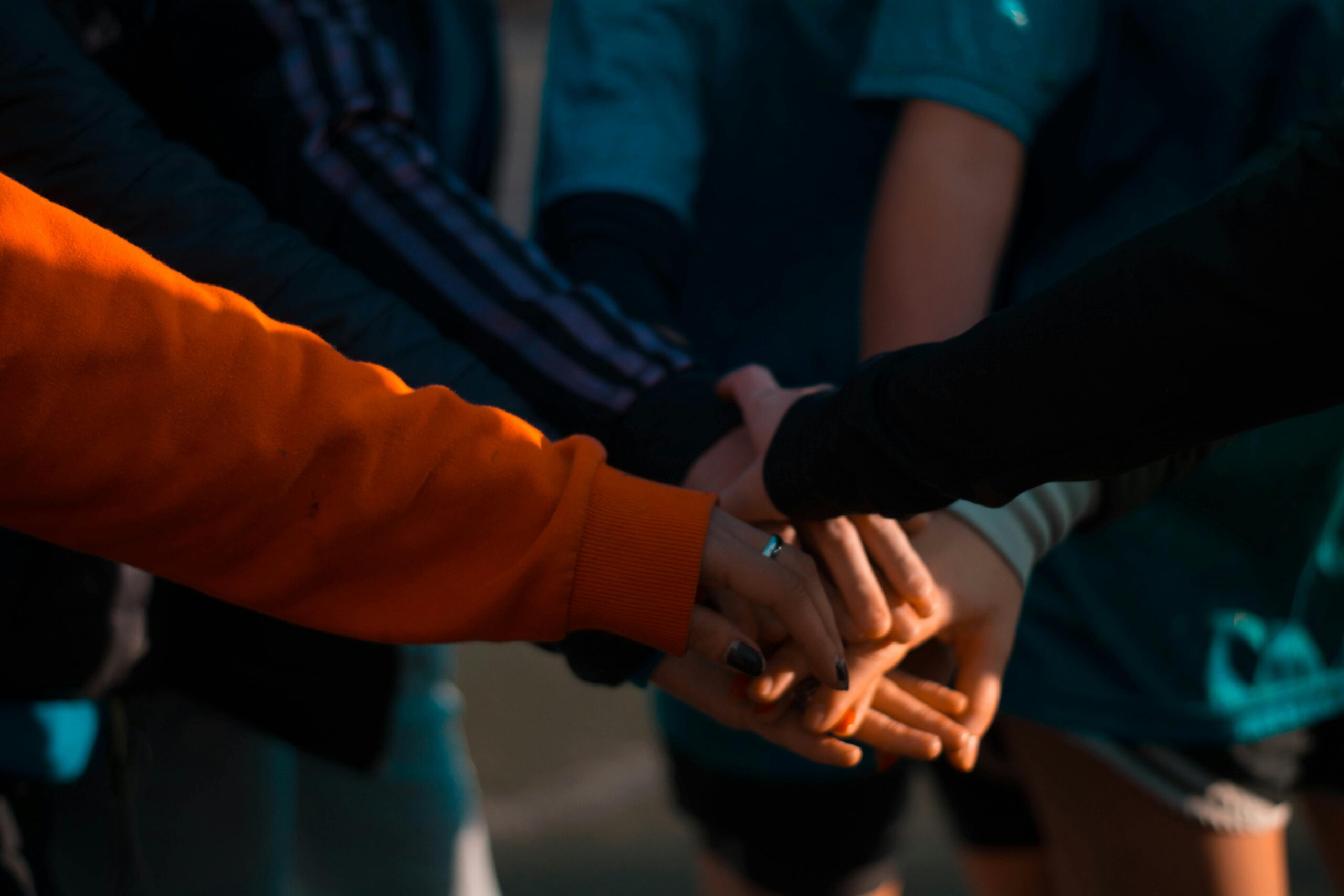 Home A close-up of diverse hands stacked together outdoors, symbolizing teamwork and unity.