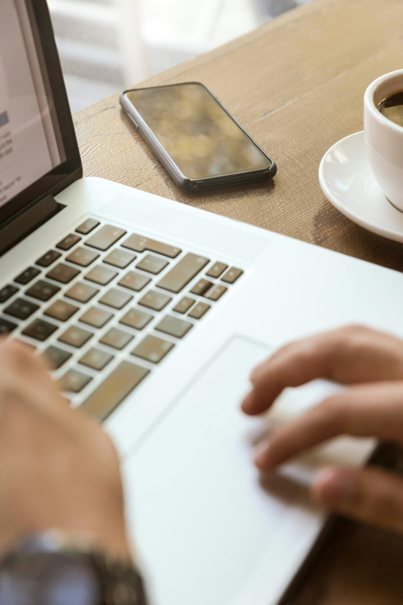TIDES Phase 1 Close-up of hands typing on a laptop with a smartphone and coffee, depicting a modern workspace.