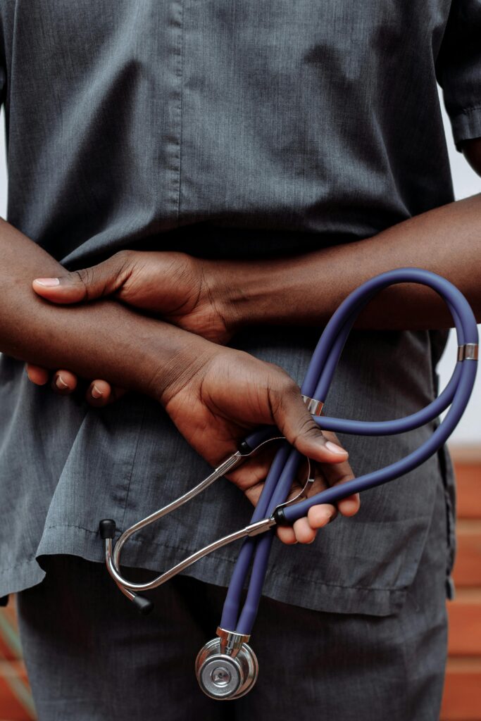 Post 2: Racism in Healthcare Medical professional in gray scrubs holding stethoscope behind back.