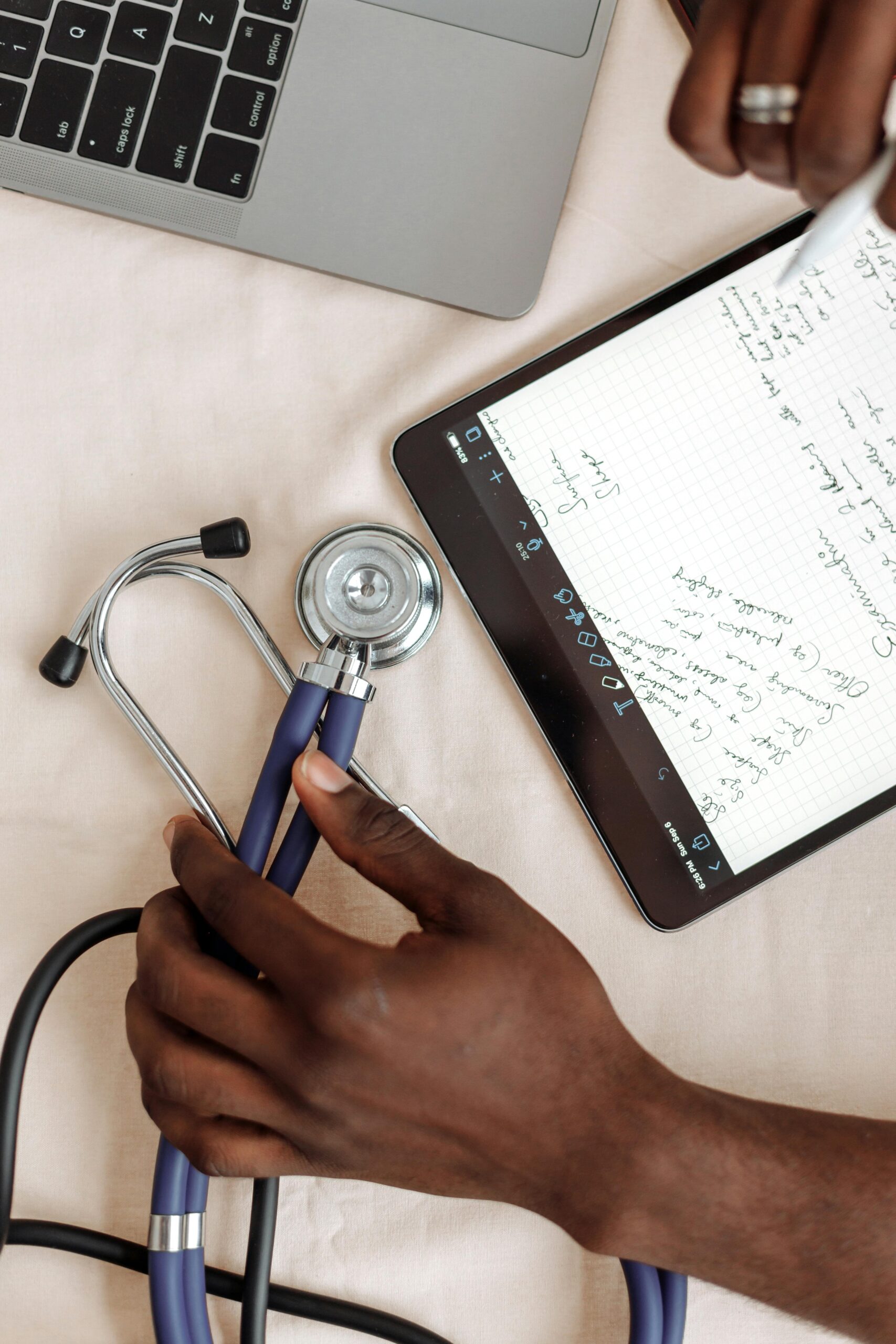 TIDES Phase 2 A close look at hands holding a stethoscope next to a tablet showing medical notes.