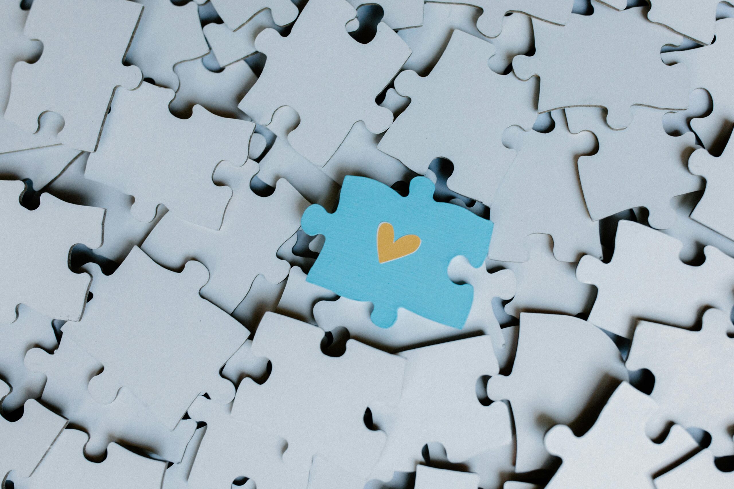 Impact A standout blue puzzle piece with a heart symbol among white puzzle pieces, showing uniqueness.